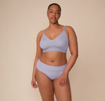 Zarria stands relaxed in a front-facing pose, modeling the Bliss Triangle Bralette in Violet and the Bliss Hiphugger in Violet. The image emphasizes the coordinated set’s sleek lines and second-skin comfort in the soft Violet color.
