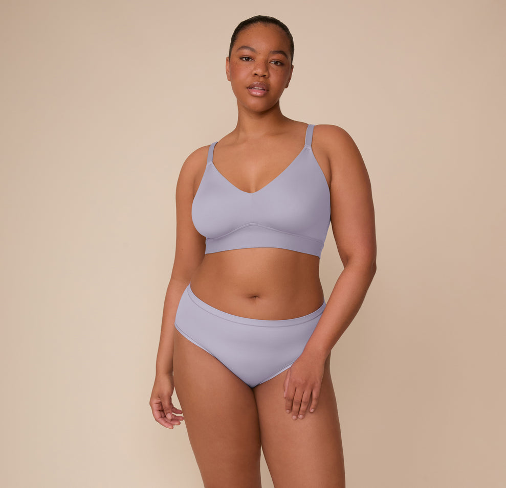 Zarria stands relaxed in a front-facing pose, modeling the Bliss Triangle Bralette in Violet and the Bliss Hiphugger in Violet. The image emphasizes the coordinated set’s sleek lines and second-skin comfort in the soft Violet color.