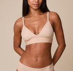 Ally wears the Bliss Triangle Bralette in Beige, showcasing the soft, wire-free cups, deep V-neckline, and supportive elastic underband against a neutral background. sizing: Ally wears size XS