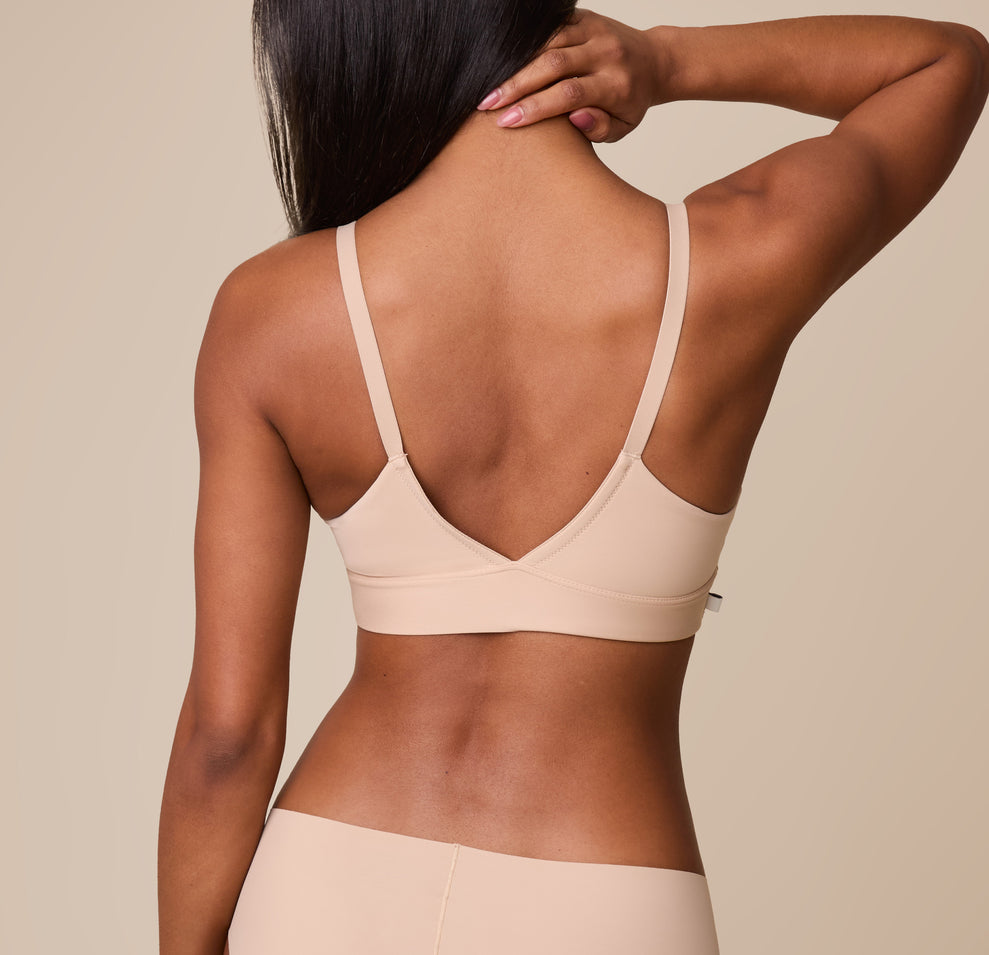 Ally turns to display the back of the Bliss Triangle Bralette in Beige, highlighting the smooth, stretchy fabric for a barely-there feel.