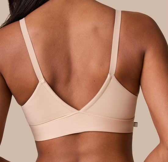 Back view of Ally wearing the Bliss Triangle Bralette in Beige. The low V back and wide, comfortable band are emphasized.