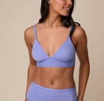 Close-up of Nemesis wearing the Bliss Triangle Bralette in Dusk. The image highlights the plunging neckline and ultra-smooth fabric of the bralette, with Nemesis smiling softly and turning slightly to her left. sizing: Nemesis wears size Medium