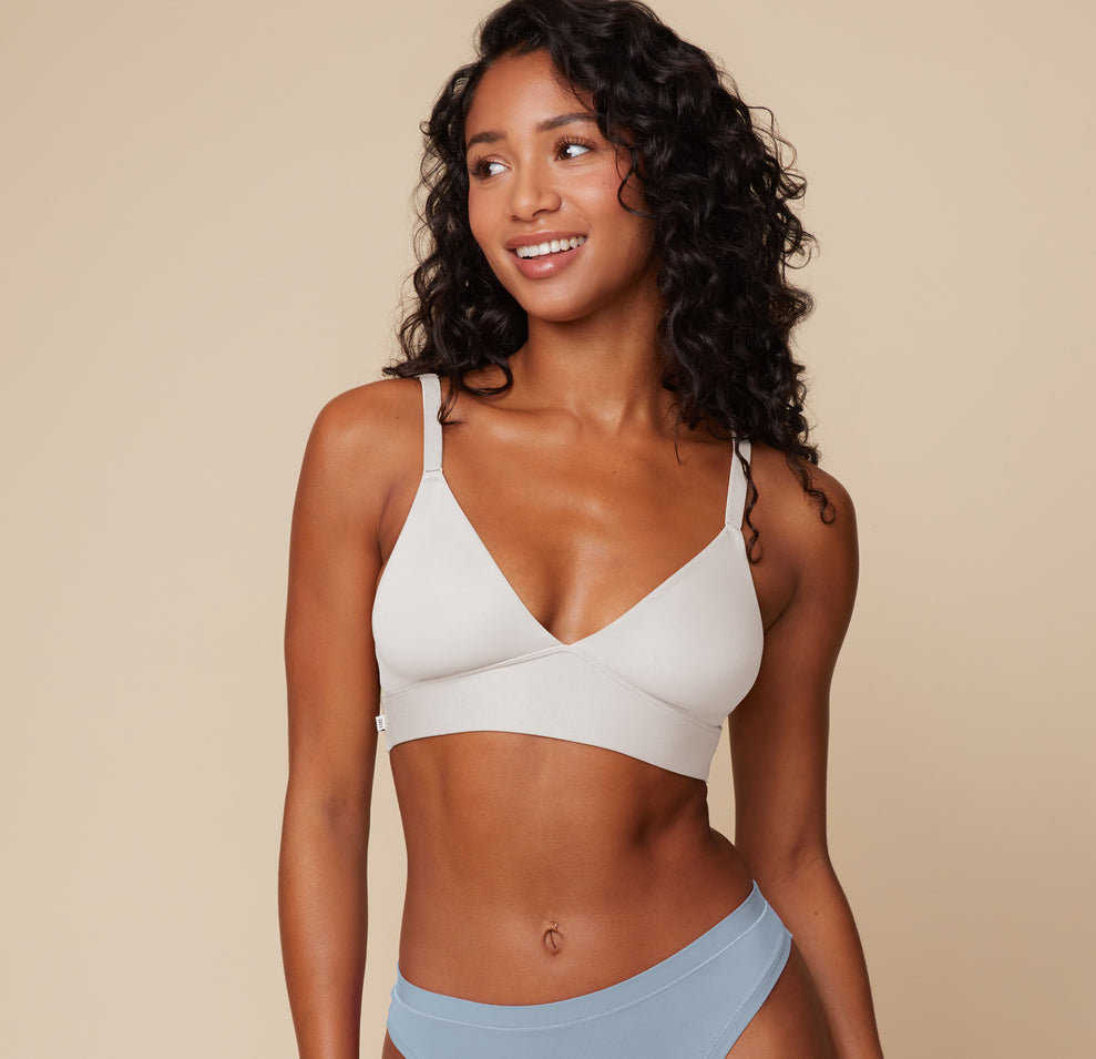 Ally wearing the Bliss Triangle Bralette in Frost. The image highlights the plunging neckline and ultra-smooth fabric of the bralette, with Ally smiling softly and turning slightly to her left. sizing: Ally wears size XS