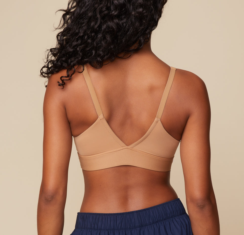 Ally poses from the back in the Bliss Triangle Bralette in Tan. The low cut V back and comfortable microfiber material are highlighted.