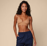 Ally wearing the Bliss Triangle Bralette in Tan, posing confidently with a soft smile. The low cut V-neck and wide underband are emphasized.
