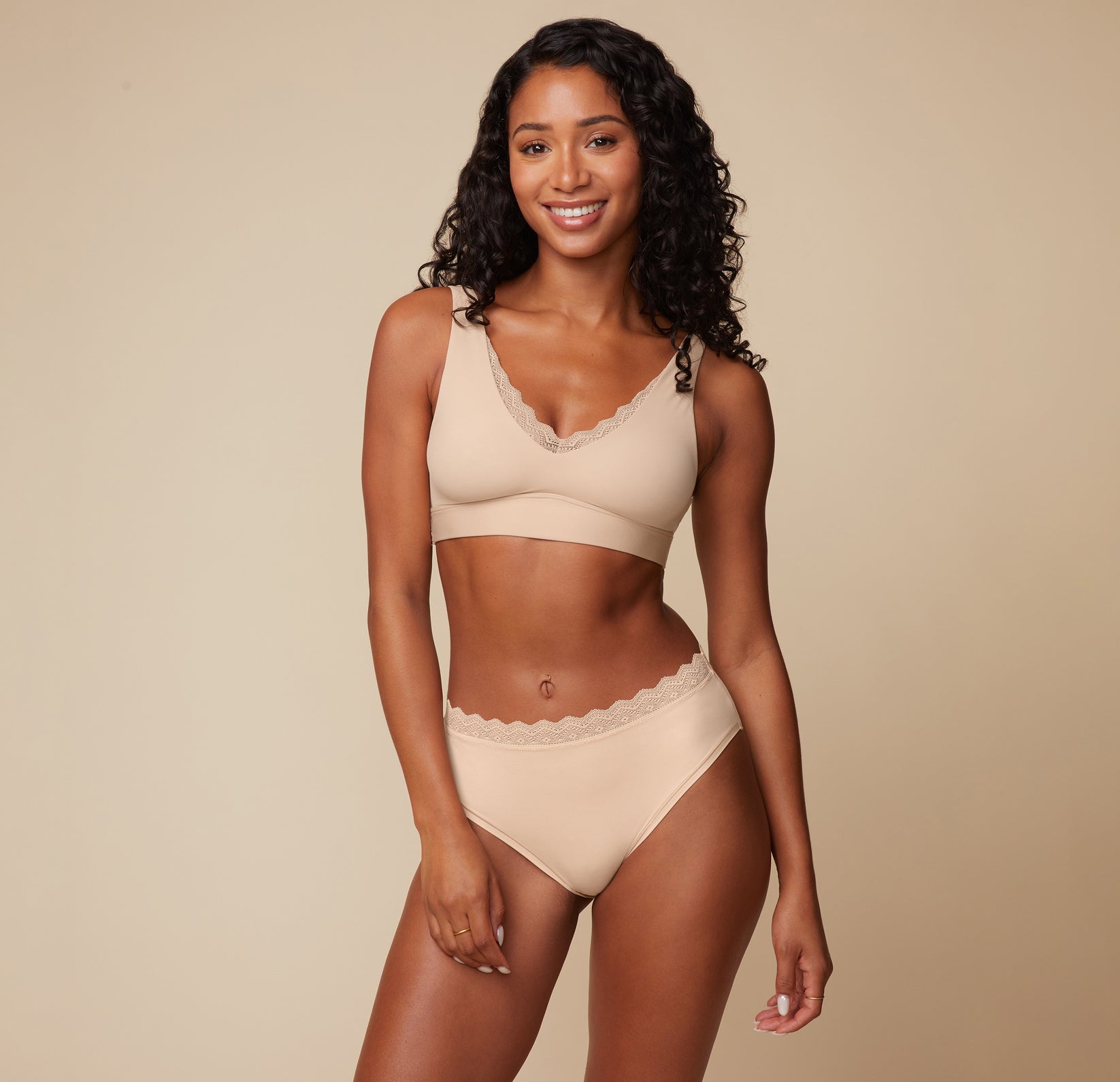 Model Ally smiling while wearing the Bliss Lace Bralette in Beige, paired with the Bliss Lace Highwaist Brief in Beige. The image highlights the bralette’s smooth, soft fabric and the high-waisted, supportive brief from the front.