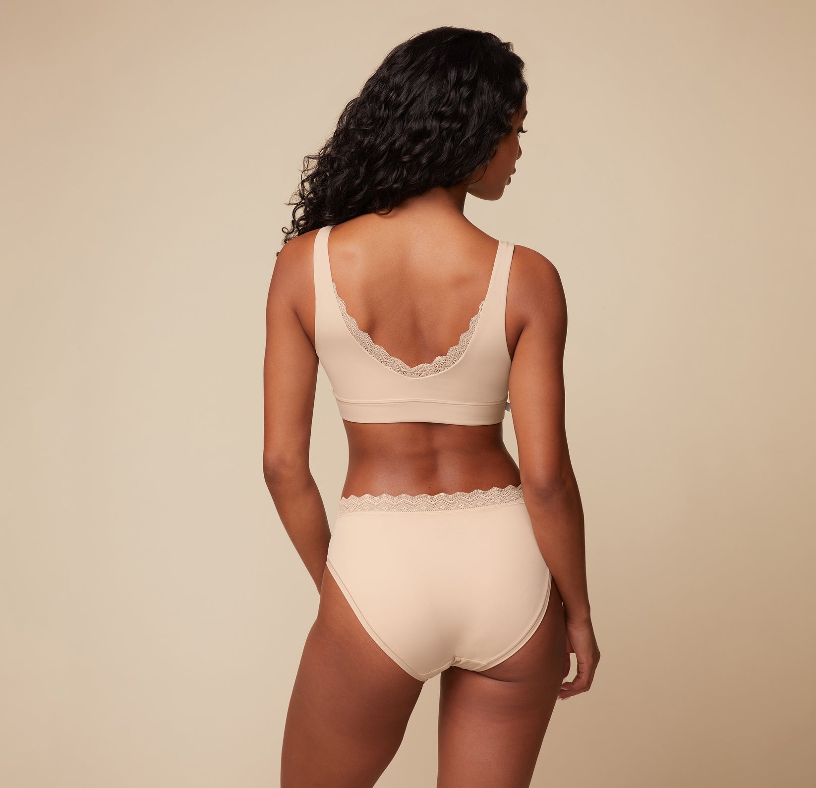 Back view of Ally wearing the Bliss Lace Bralette and Bliss Lace Highwaist Brief in Beige.
