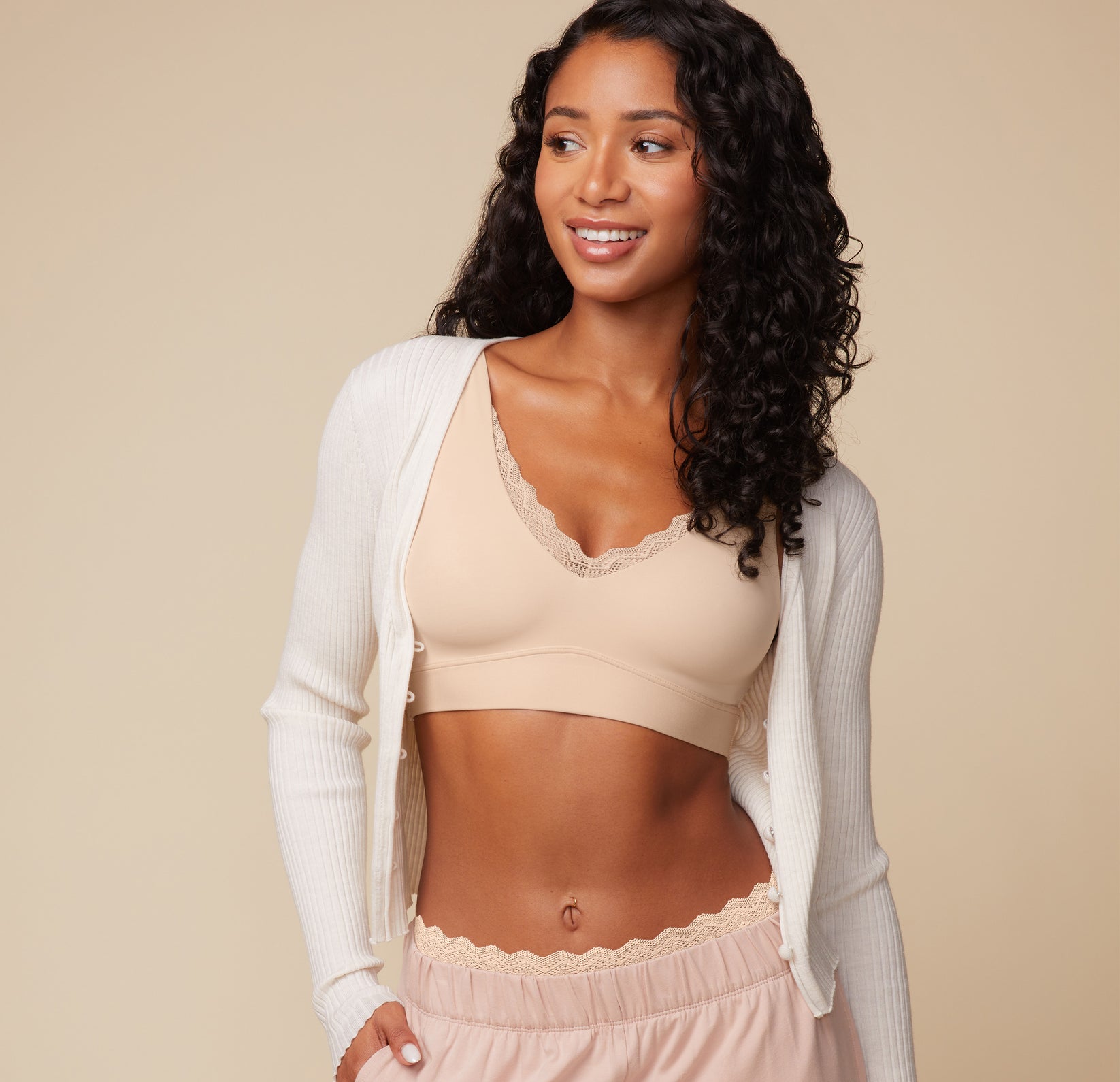 Ally wearing the Bliss Lace Bralette in Beige paired with cozy loungewear. She smiles while wearing a light cardigan, emphasizing the versatility and comfort of the bralette.