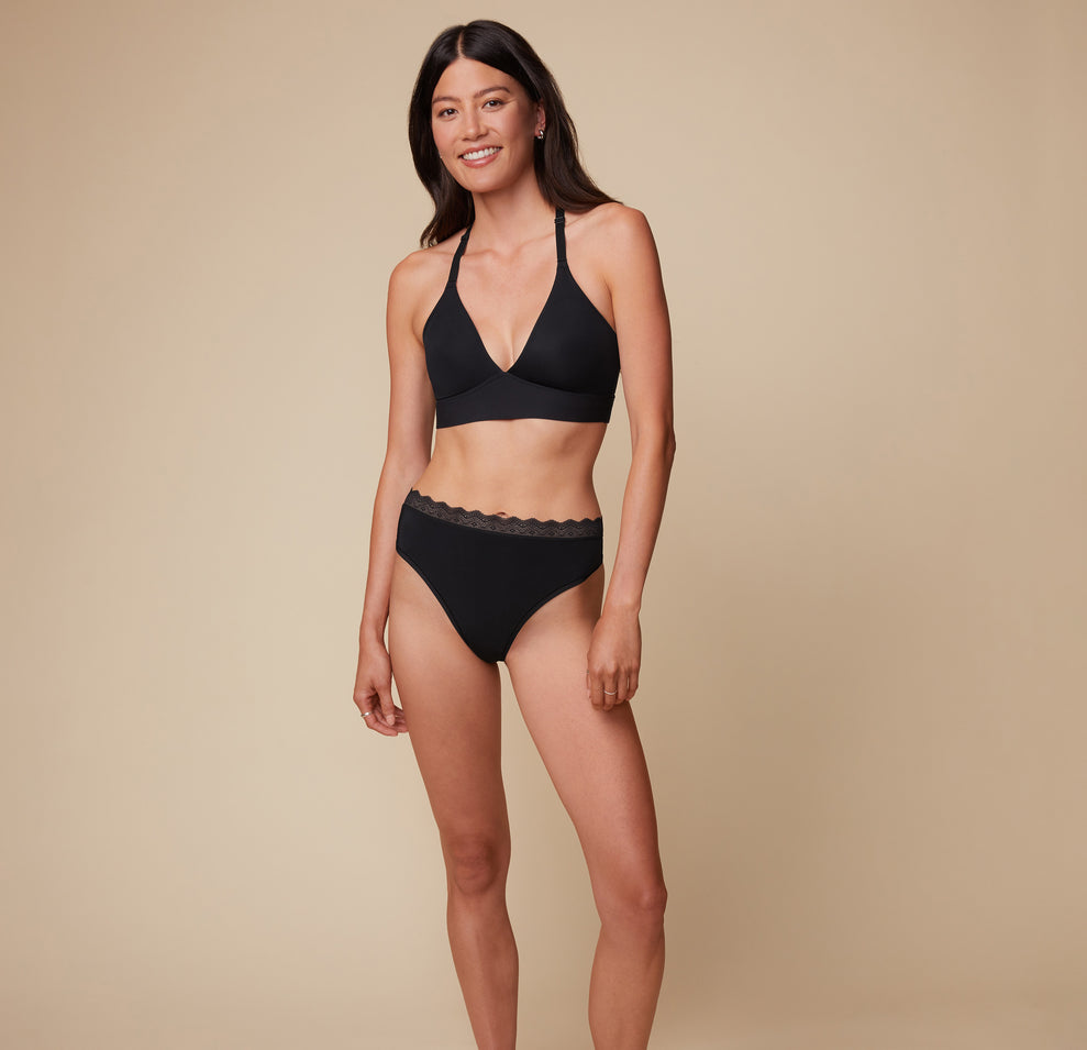 Model Anna wearing the Bliss Lace Halterneck Bralette in Black, paired with the matching Bliss Highwaist Lace Thong. She stands facing forward, showcasing the supportive fit of the halterneck bralette and the sleek design of the highwaist thong. sizing: Sizes L-4XL have higher center in front for additional support.