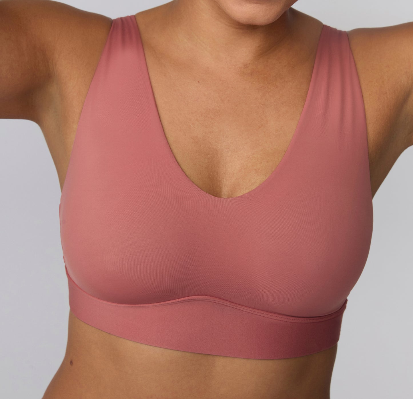 On a light studio backdrop, a close-up shows India wearing the Bliss Bralette in Cinnamon, highlighting the scoop neckline, smooth microfiber fabric, and wide wireless band designed for comfortable support.
