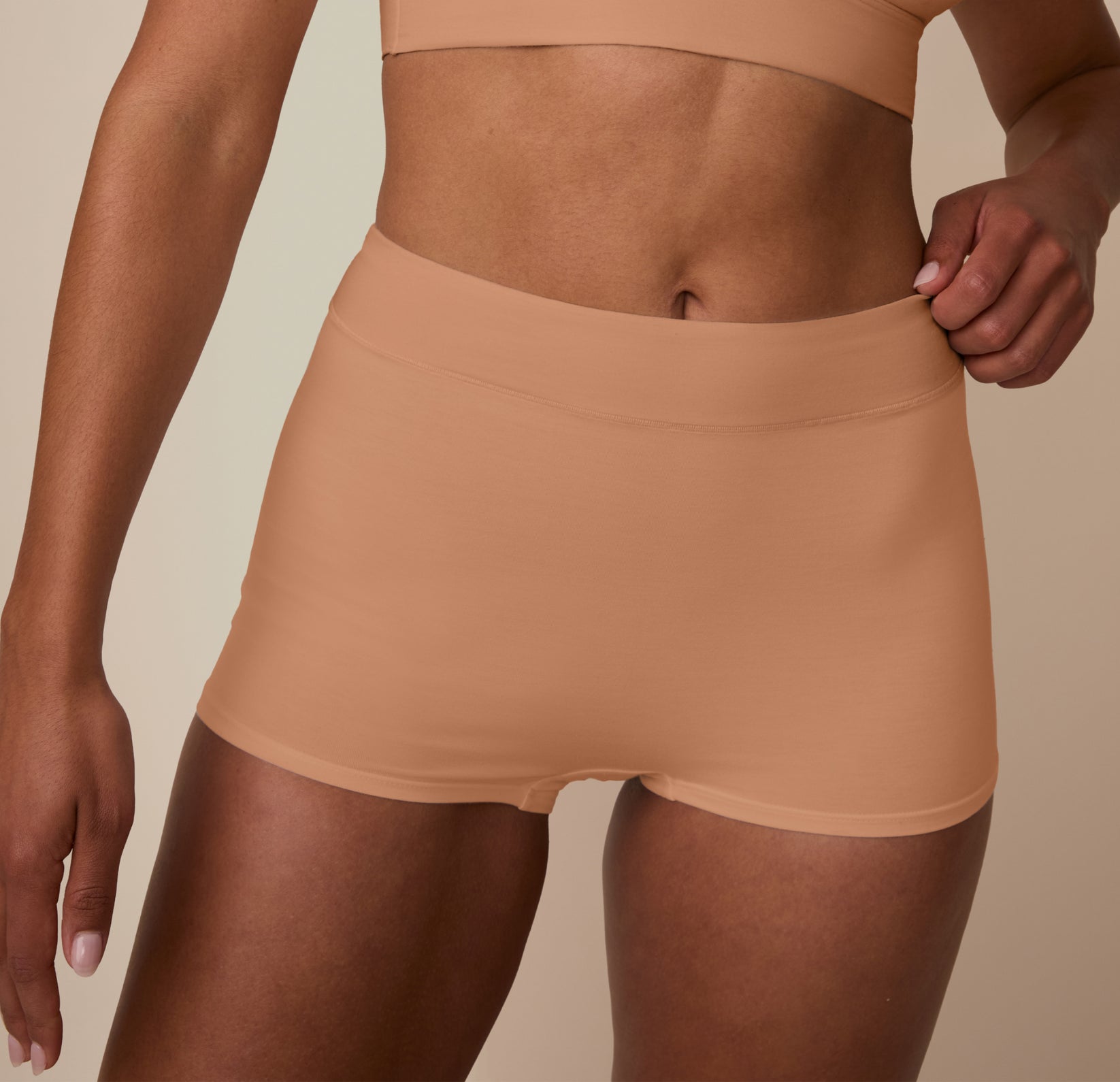 Close-up of Nemesis adjusting the waistband of the Cloud Cotton High Waist Boyshort in Dune. The image focuses on the soft-stretch fabric and flexible waistband designed for all-day wear.