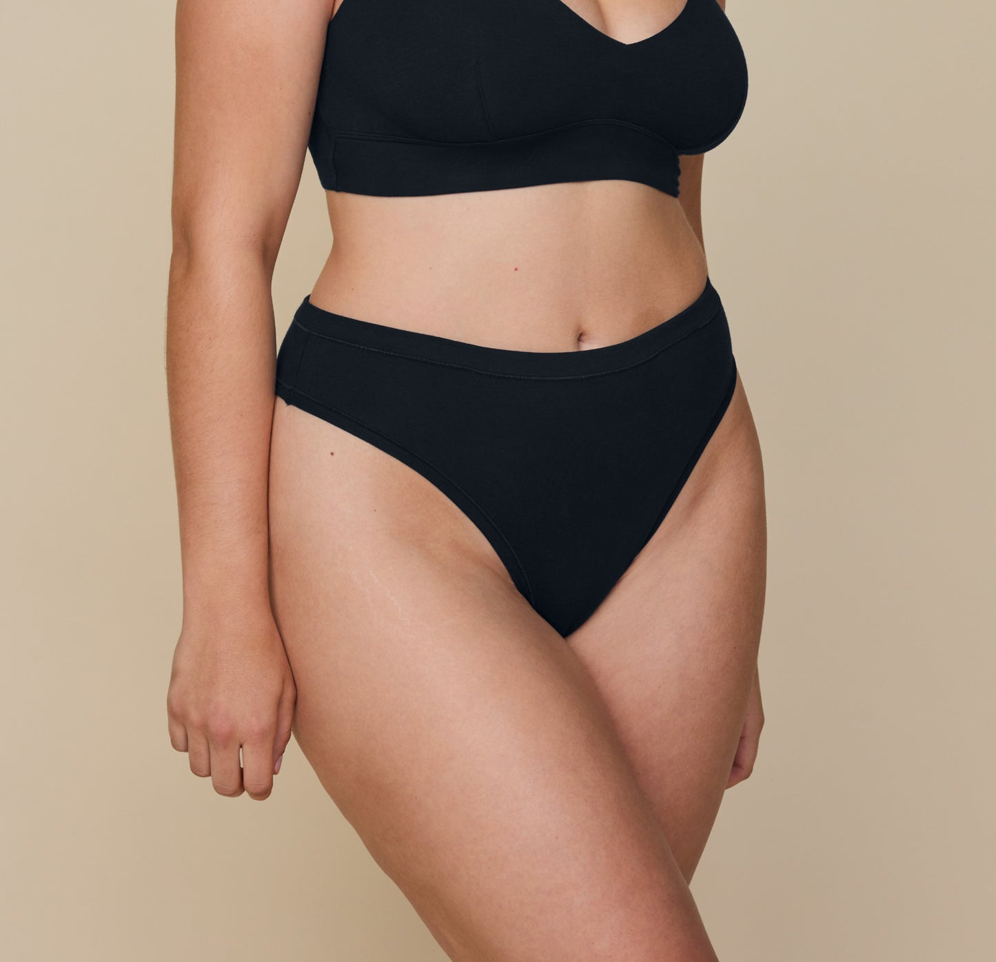 Angled view of Summerlyn wearing the Cloud Cotton Highwaist Thong in Black. The image highlights the high-rise waistband and smooth, stretchy fit with minimal front coverage. sizing: Summerlyn wears size Large