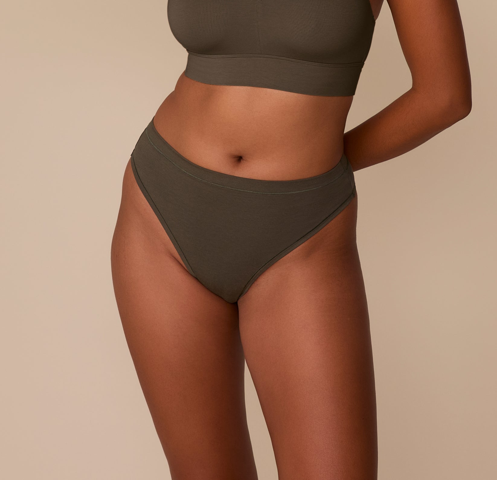 Victoria wearing the Cloud Cotton Highwaist Thong in Olive, shown from the front with a high-rise waistband and minimal coverage. sizing: Victoria wears size Medium