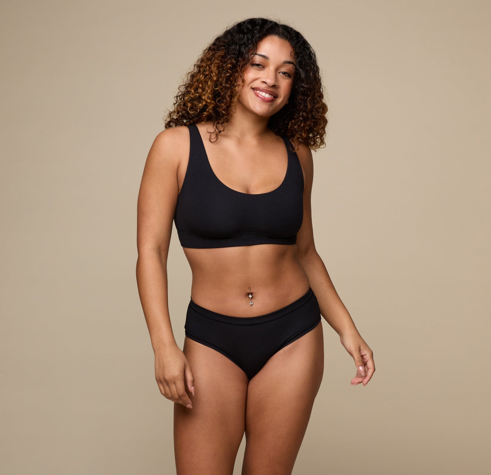 Full body view of Jade wearing the Cloud Cotton Scoop Bralette and the Cloud Cotton Hiphugger in Black. She smiles casually with her arms naturally by her sides against a neutral background.