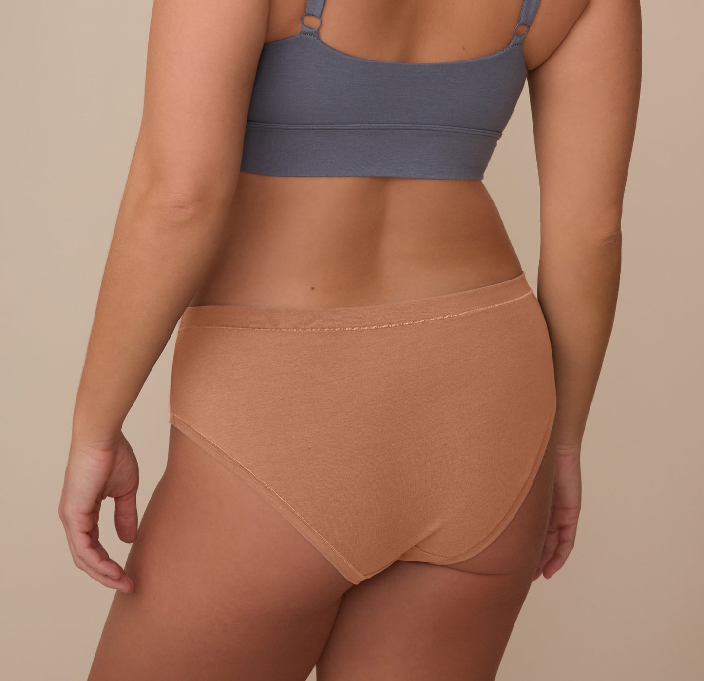 Back view of model Sonnie wearing the Cloud Cotton Hiphugger in Dune. The image highlights the full back coverage and comfortable waistband that stays in place without digging.
