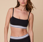 A close-up of Gracie wearing the Cloud Cotton Retro Bandeau Bralette in Black. The minimalist design features a straight neckline, thin adjustable straps, and a sporty elastic underband with contrast white stripes. sizing: Gracie wears size Small