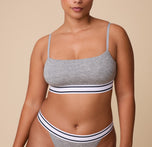 India wears the Cloud Cotton Retro Bandeau Bralette in Heather Charcoal, featuring a soft, square neckline with thin, adjustable straps. The elastic underband with a striped design provides a snug, sporty fit. sizing: India wears size Large