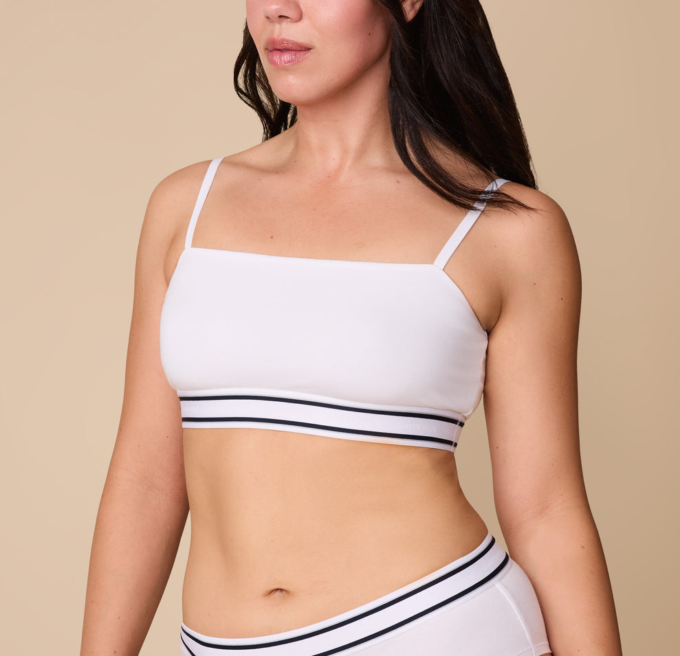 A close-up of Emersyn wearing the Cloud Cotton Retro Bandeau Bralette in White. The straight neckline and thin adjustable straps offer a sleek and minimal look, while the striped elastic underband adds a sporty touch. sizing: Emersyn wears size Large