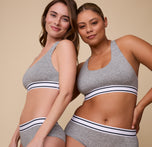 India and Gracie standing side by side, both wearing the Cloud Cotton Retro Racerback Bralette in Heather Charcoal, paired with the coordinating Hiphugger. The image highlights how the bralette looks on different skin tones and body types.