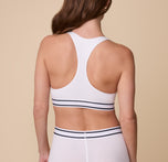 The back view of Gracie wearing the Cloud Cotton Retro Racerback Bralette in White, highlighting the racerback design for enhanced support and mobility. The soft cotton fabric and wide elastic underband are showcased.