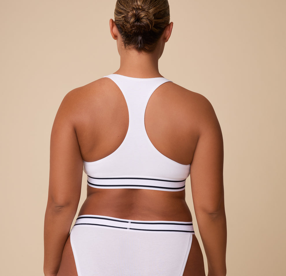 India showcases the racerback style from behind, highlighting the contoured shape and supportive fit of the Cloud Cotton Retro Racerback Bralette in White.