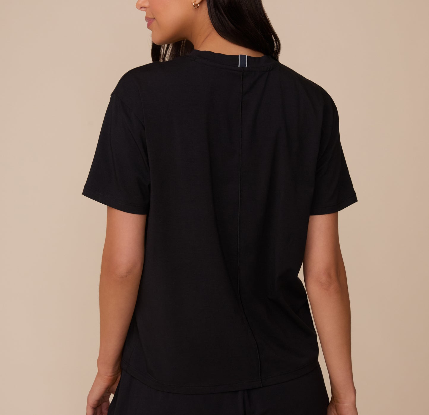 Back view of Marcela wearing the Cloud Cotton T-Shirt in Black. The shirt features a center seam detail and a relaxed fit through the shoulders and torso.