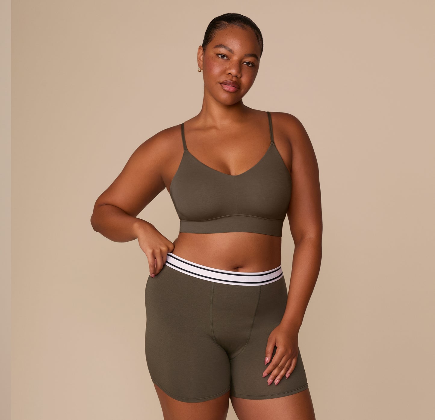 Zarria in the Cloud Cotton Triangle Bralette in Olive paired with the matching Cloud Cotton Retro Boxer Brief, standing with one hand resting on the waistband to show the branded elastic band.