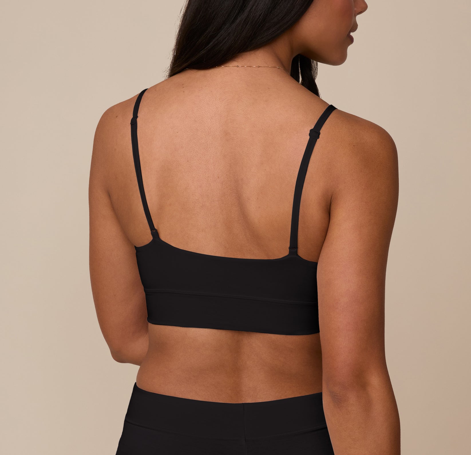 Nemesis turned away from the camera, wearing the Cloud Cotton Triangle Bralette in Black. The back shows the scoop shape and slim, adjustable straps that lay flat against the skin.