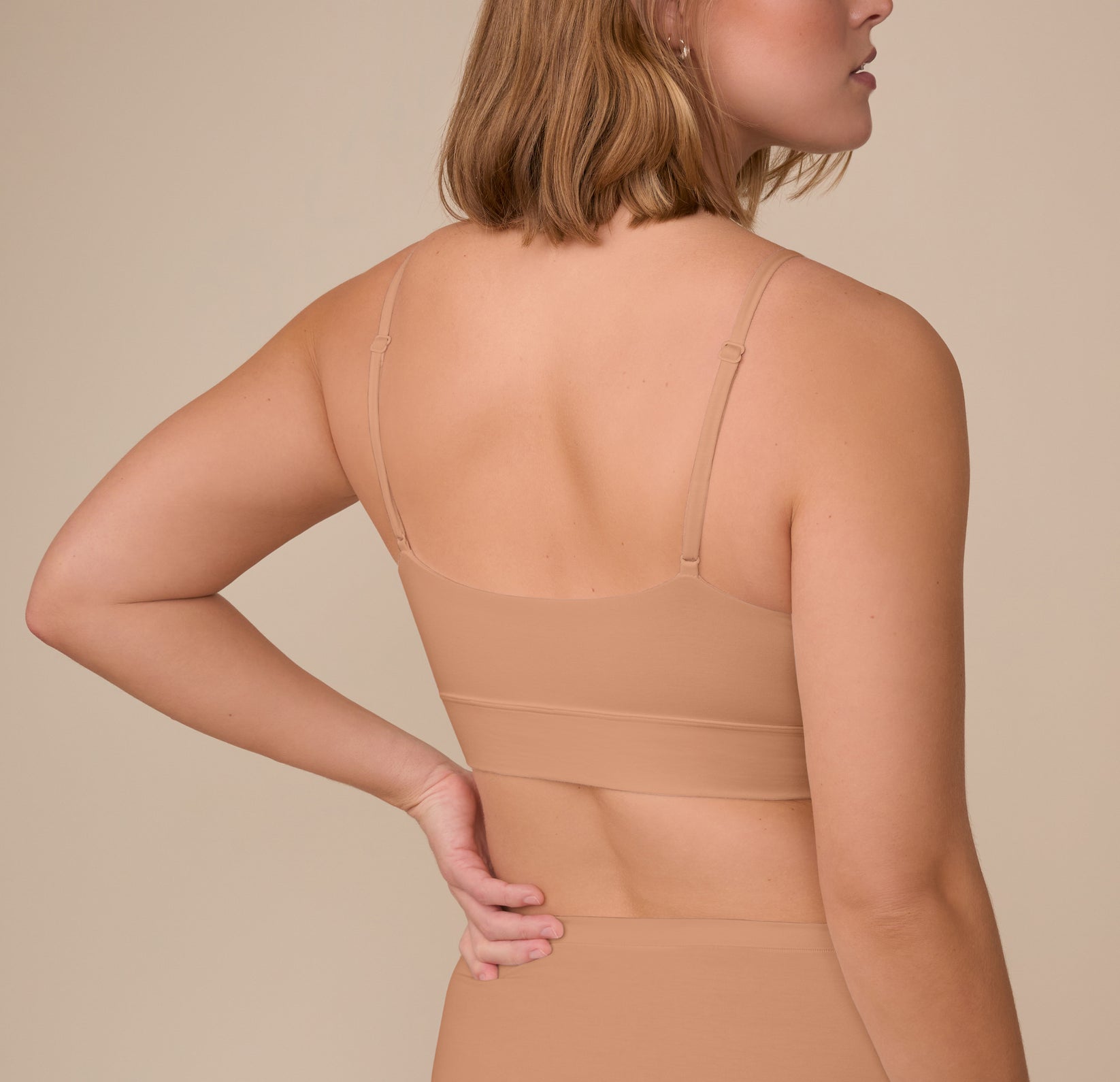 Sonnie shown from the back wearing the Cloud Cotton Triangle Bralette in Dune. The smooth scoop-back design and slender, adjustable straps ensure a flexible, stay-put fit.