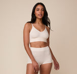 Full-body front view of model Nemesis wearing the Cloud Cotton Triangle Bralette and matching Cloud Cotton Boyshort in Quartz. The image conveys a sense of effortless comfort and lounge-ready ease.