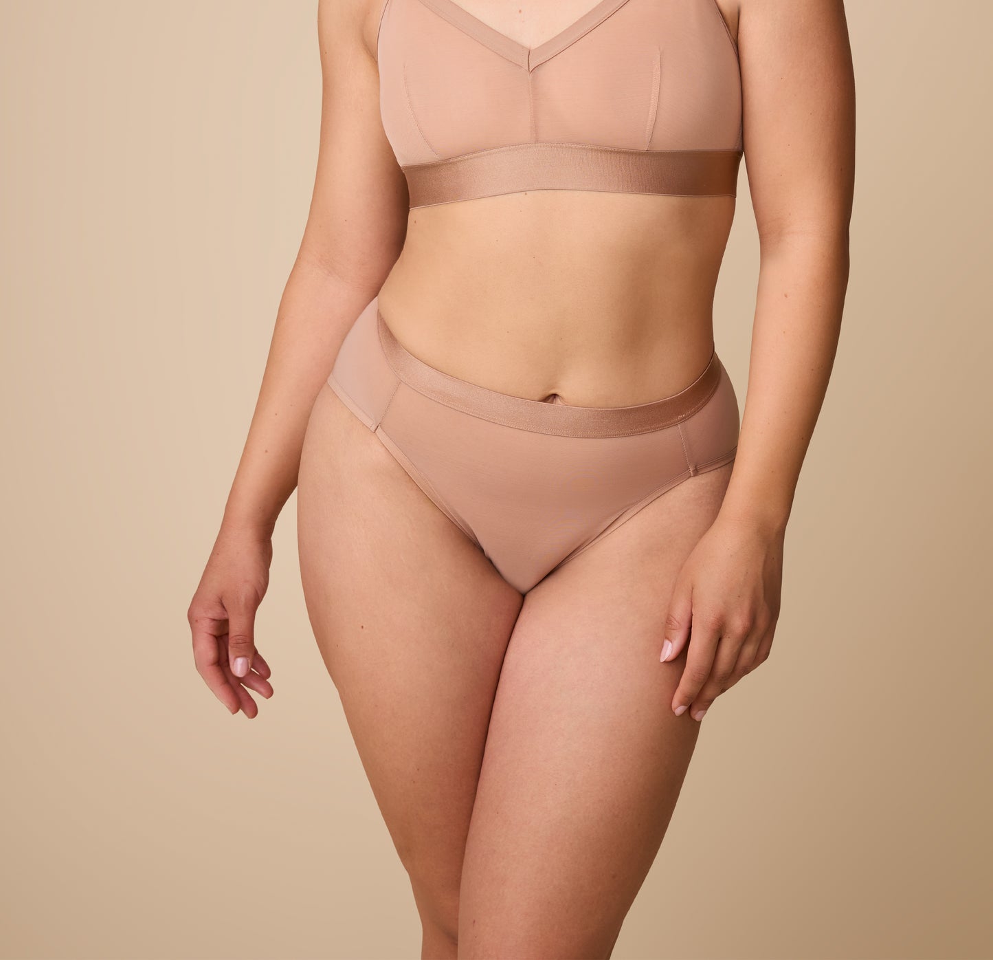 A close-up of a model wearing taupe highwaist briefs made from ComfortMesh™ fabric. The design features flattering front seams and a wide waistband that provides a smooth and supportive fit. The high-leg cut accentuates the natural contours of the body.