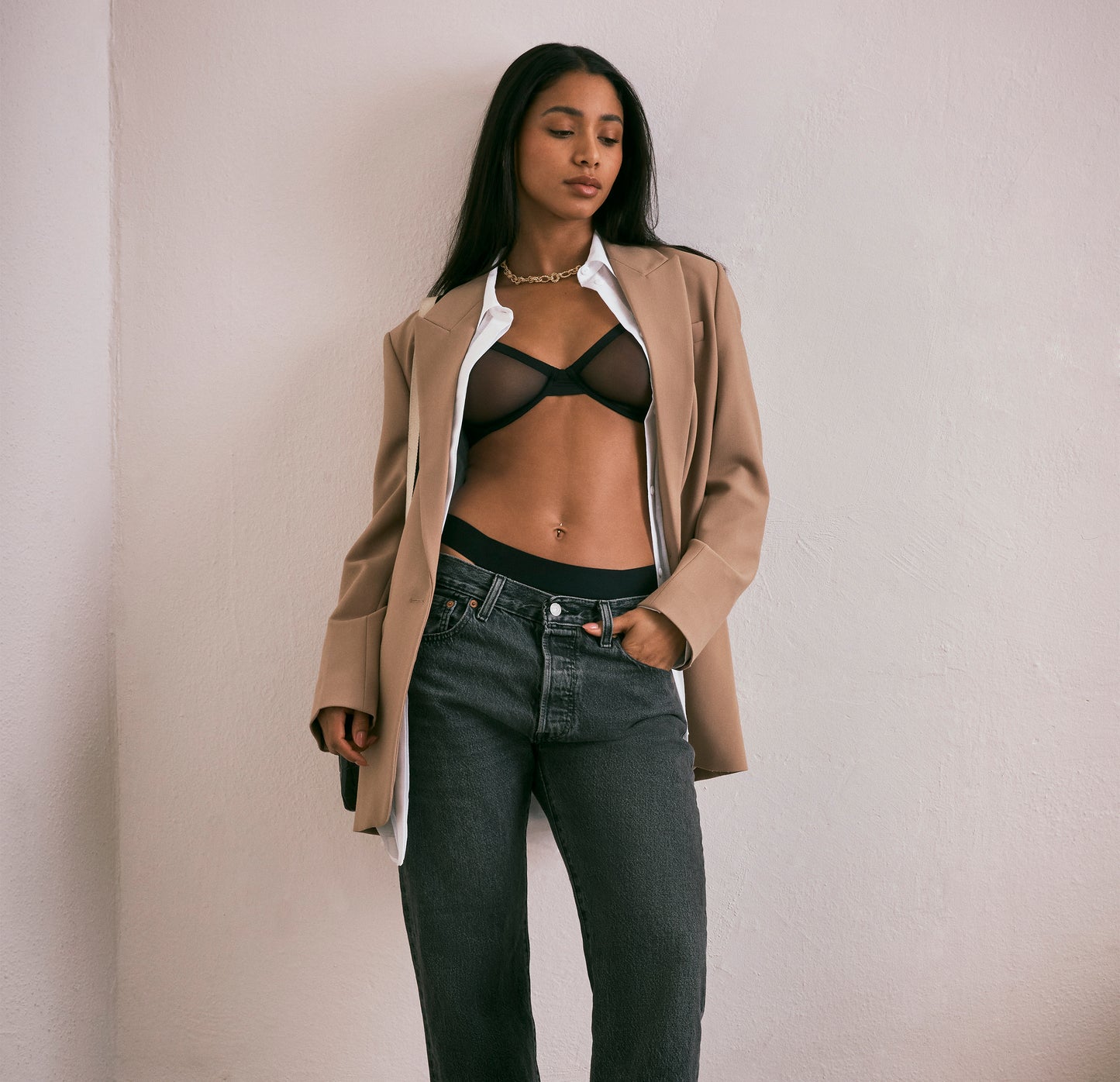 Ally confidently wearing the ComfortMesh Plunge Bra in Black, styled under a beige blazer with a white shirt and jeans, perfect for versatile day-to-night wear.