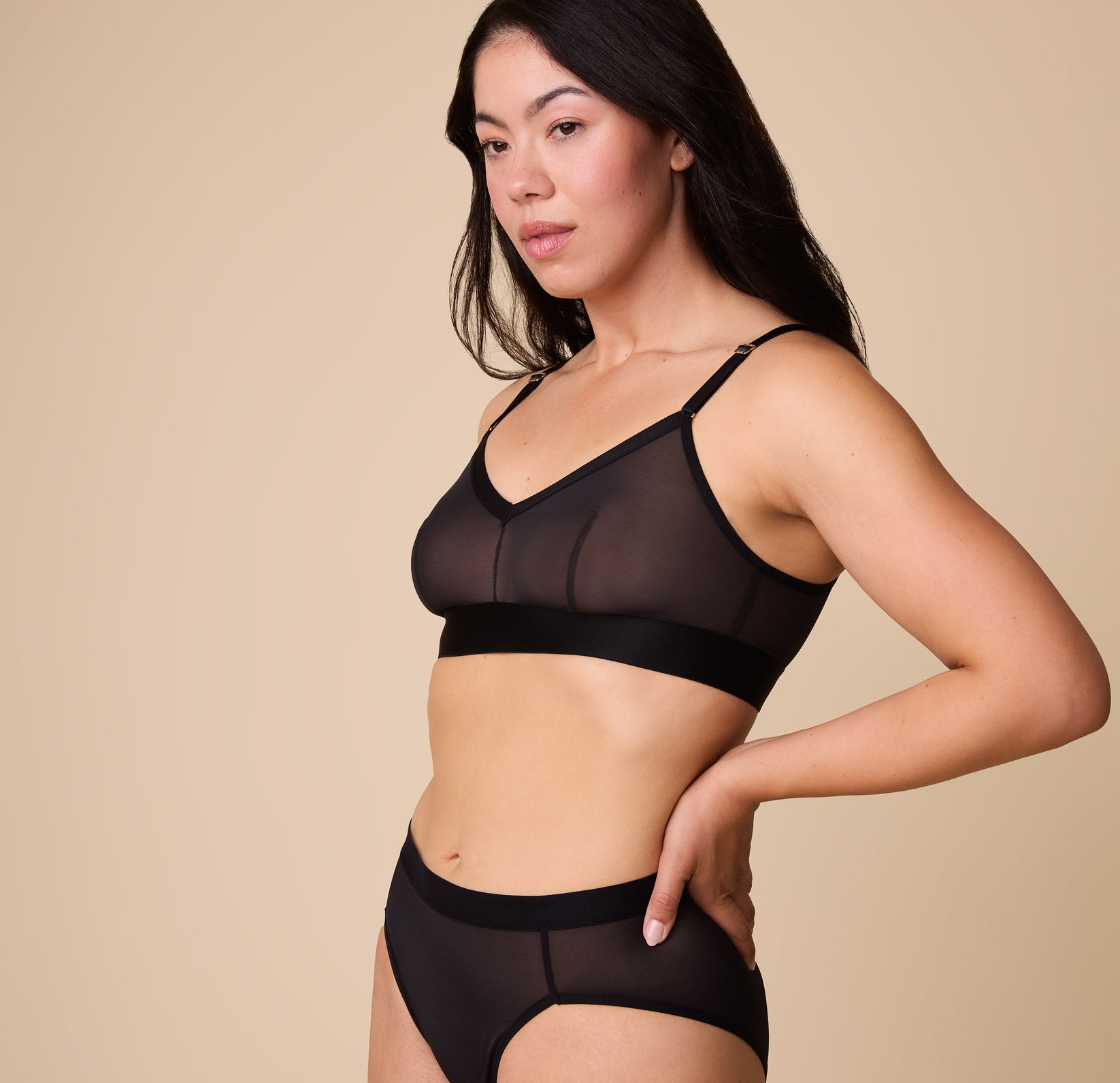 A three quarter view of Emersyn wearing the ComfortMesh Triangle Bralette in Black with matching high-waist bottoms, emphasizing the bralette’s sleek fit and supportive design.