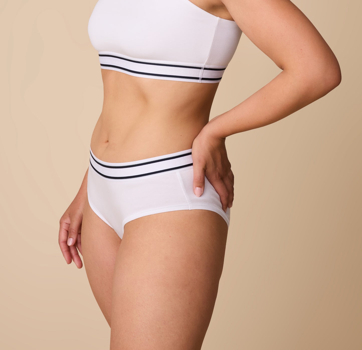 A three quarters view of Emersyn wearing the Cloud Cotton Retro Hiphugger in White, with a hand on her hip, emphasizing the smooth, stretch fit.