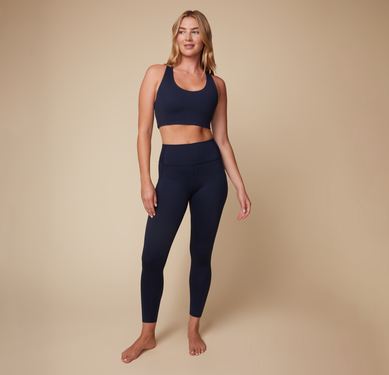 Full body view of Megan wearing the Flex Convertible Sports Bra and High Rise Legging in Ink. The matching set molds comfortably to the body.
