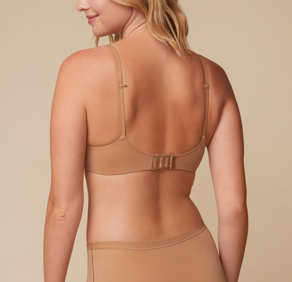 Back view of Megan wearing the Base Wirefree T-Shirt Bra in Tan. The image highlights the adjustable straps, racerback function, hook-and-eye closure for added support and comfort.