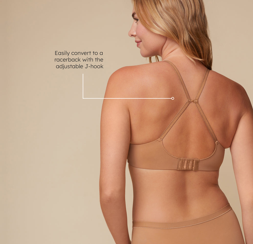 Back view of Megan wearing the Base Wirefree T-Shirt Bra in Tan, demonstrating the J-hook feature that allows for a racerback conversion. A tagline reads, "Easily convert to a racerback with the adjustable J-hook".