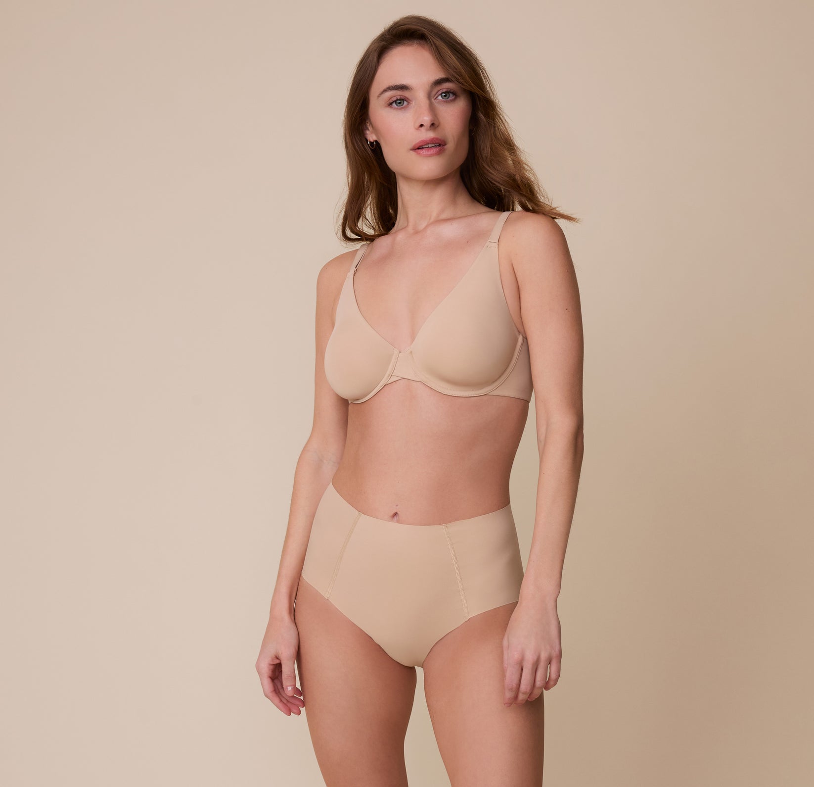 Gracie wears the No-Show Highwaist Brief in Beige, paired with the matching Base Unlined Bra, standing against a neutral background with a soft expression.