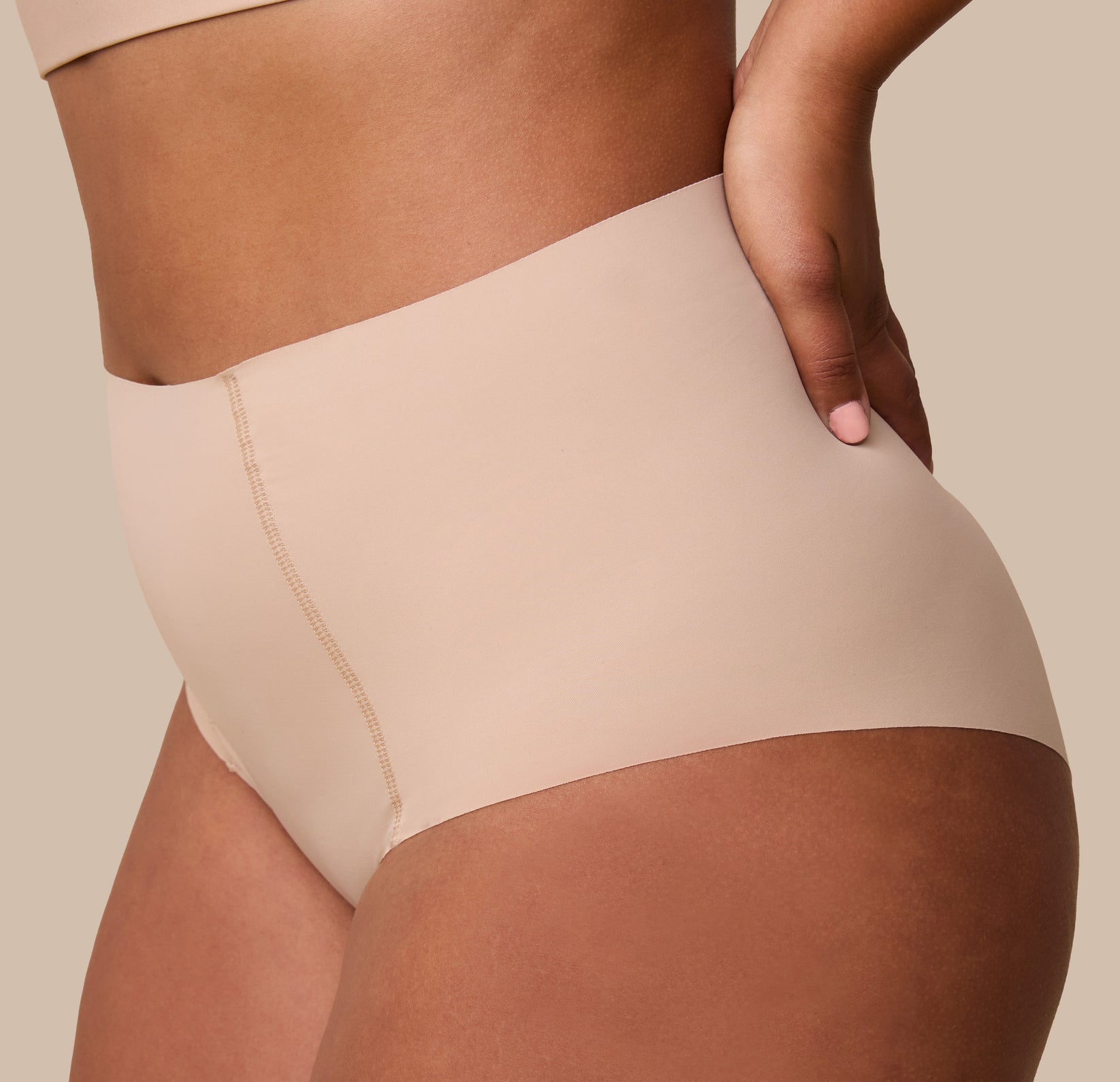 A close-up of India gently resting her hand on her hip while wearing the No-Show Highwaist Brief in Beige, showcasing the soft, elastic-free waistband.