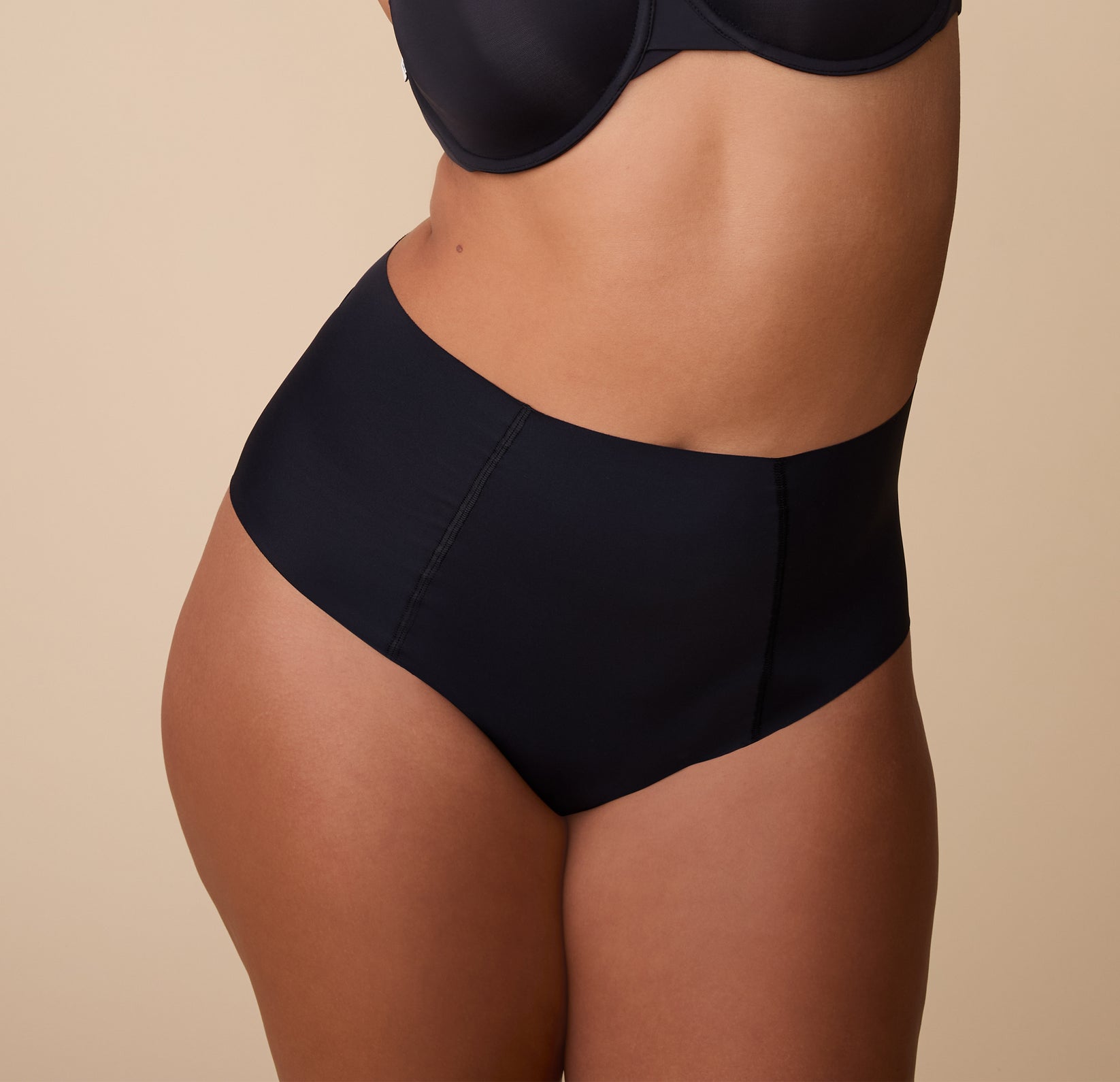 A close-up of India wearing the No-Show Highwaist Brief in Black. The seamless, high-waisted design creates a smooth, invisible look under clothing. sizing: India wears size Large