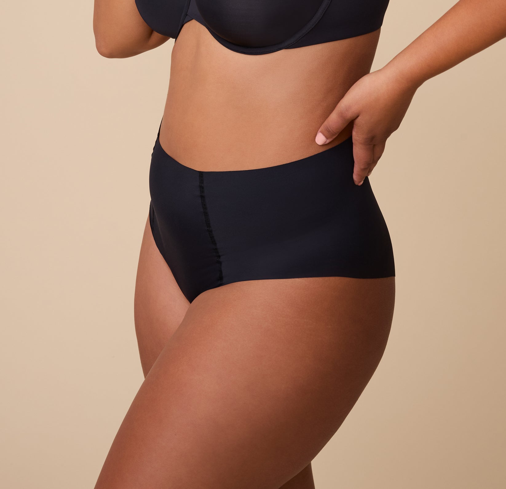 A side profile of India in the No-Show Highwaist Brief in Black, with her hand resting on her hip, emphasizing the soft, elastic-free waistband.
