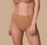 A close-up of Gracie wearing the No-Show Highwaist Brief in Tan. The seamless, high-waisted design offers a smooth, invisible fit under clothing. sizing: Gracie wears size Small