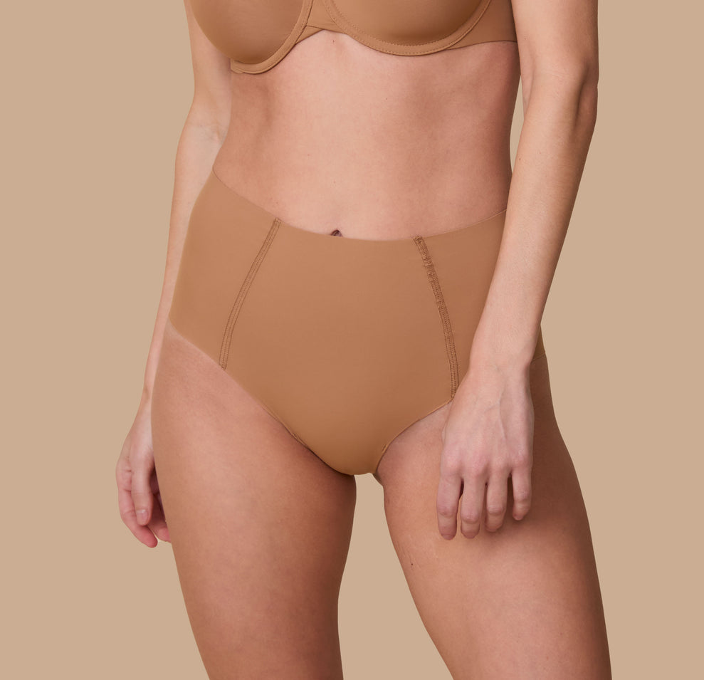 A close-up of Gracie wearing the No-Show Highwaist Brief in Tan. The seamless, high-waisted design offers a smooth, invisible fit under clothing. sizing: Gracie wears size Small