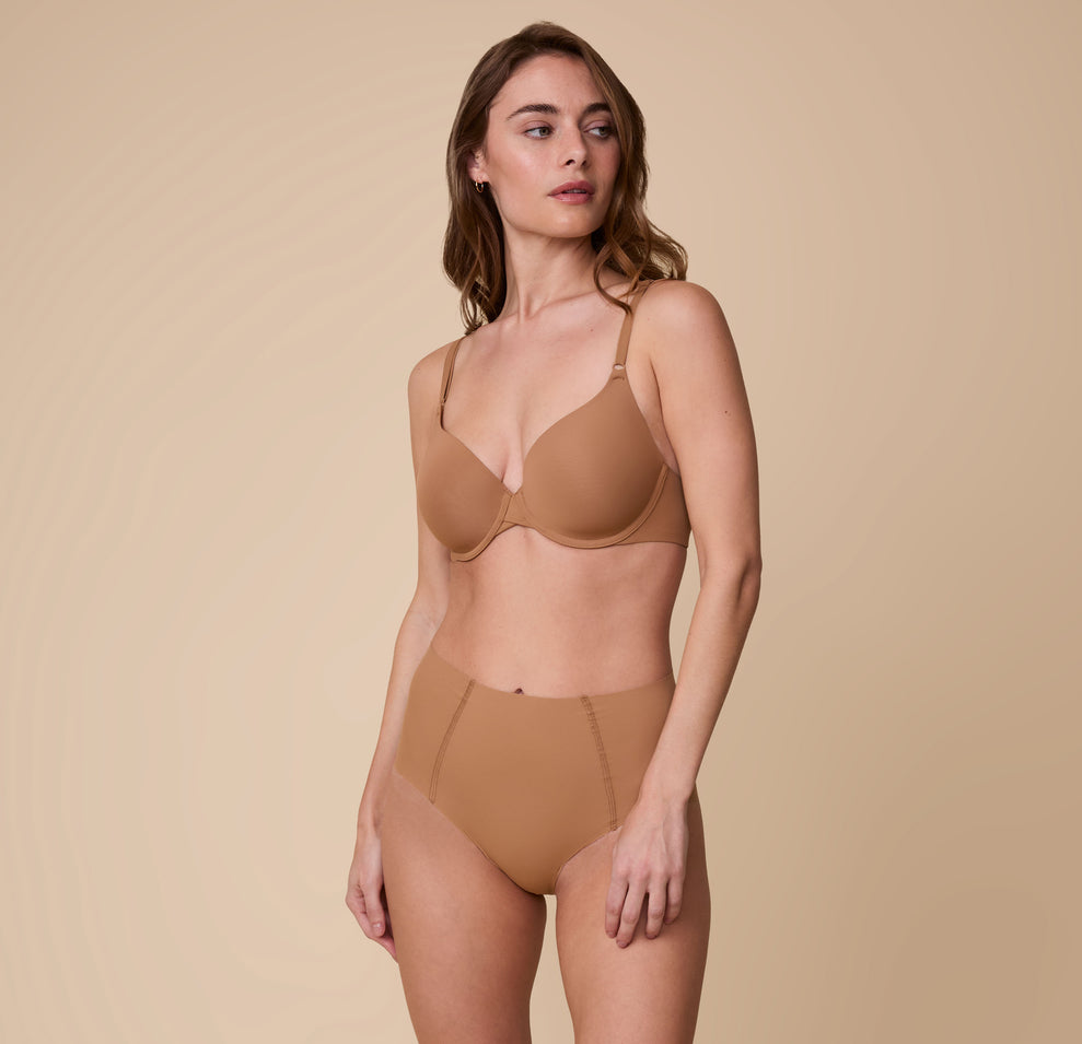 Gracie wears the No-Show Highwaist Brief in Tan, paired with the matching Base T-Shirt Bra, standing against a neutral background with a relaxed expression.
