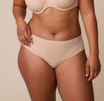 A close-up of India wearing the No-Show Hiphugger in Beige. The seamless design and mid-rise fit create a smooth, invisible look under clothing. sizing: India wears size Large