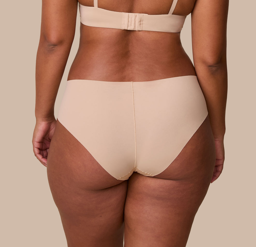 India is shown from behind, highlighting the full-coverage back and raw-cut edges of the No-Show Hiphugger in Beige for a sleek, no-show finish.