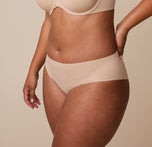 A side profile of India in the No-Show Hiphugger in Beige, with her hand resting on her hip, emphasizing the soft, elastic-free waistband.