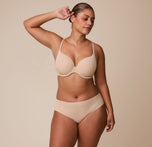 India wears the No-Show Hiphugger in Beige, paired with the matching Base T-Shirt Bra, standing against a neutral background with a confident, relaxed expression.