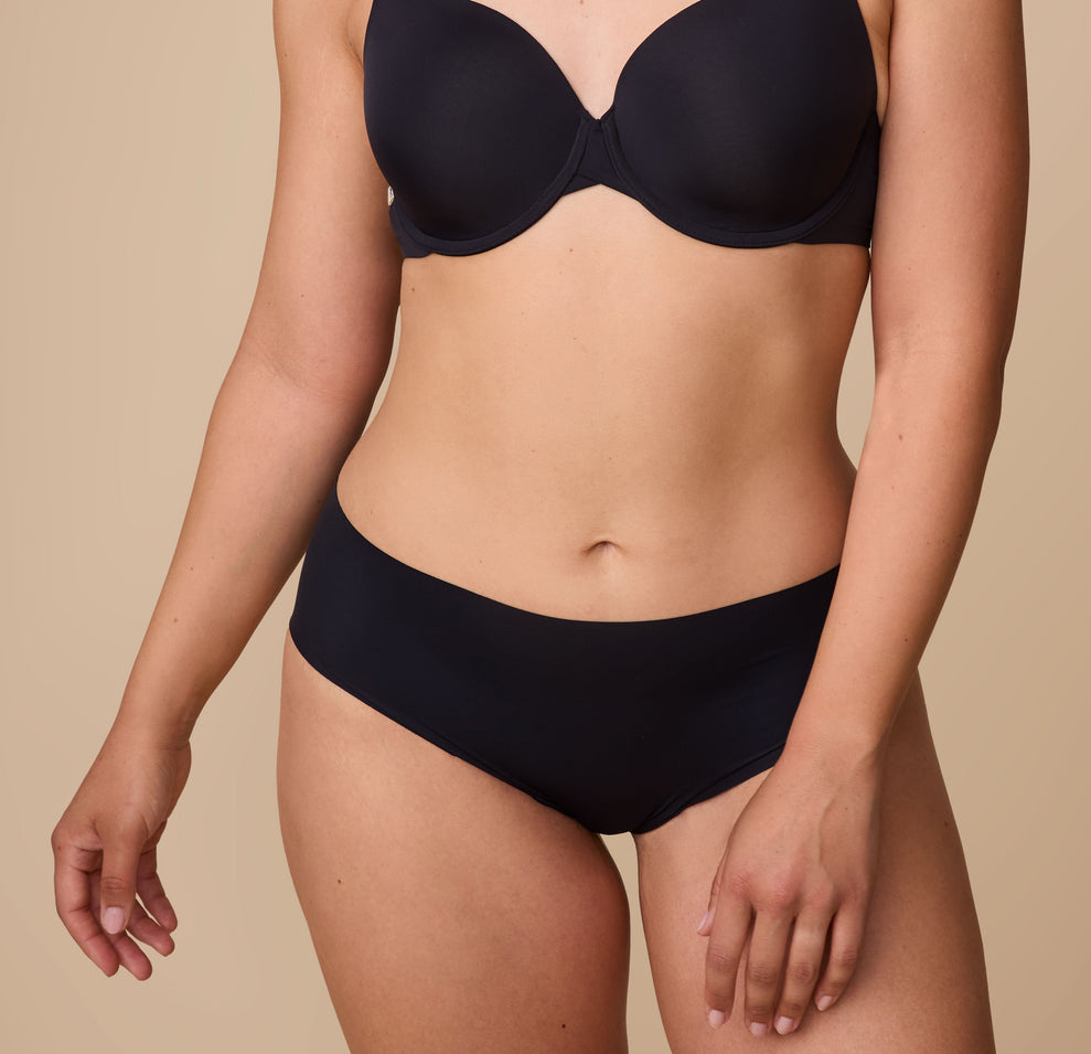 A natural movement shot of Emersyn in the No-Show Hiphugger in Black paired with the matching Base T-Shirt Bra, highlighting the effortless comfort and barely-there feel of the design. sizing: Emersyn wears size Large