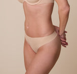 Gracie modeling the No-Show Thong in Beige at a three quarter angle.The soft, stretch fabric hugs her body for a barely-there feel.